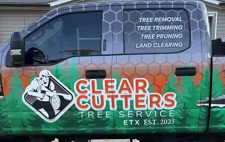 Door and rear window of the Clear Cutters F-250: the logo, CLEAR CUTTERS TREE SERVICE ETX EST. 2023, and TREE REMOVAL, TREE TRIMMING, TREE PRUNING, LAND CLEARING lettered on the glass